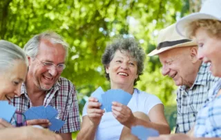 Five older people happily play cards outside.
