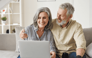 An older couple smiles at a laptop screen as they sit together.