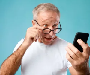 An older man looks at his phone in surprise. 