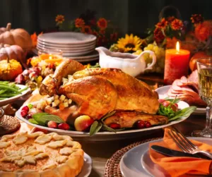 A holiday table showing a turkey, a pie, candles, and white china. 