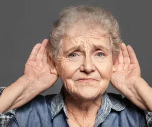 An older woman cups her hands around her ears. 