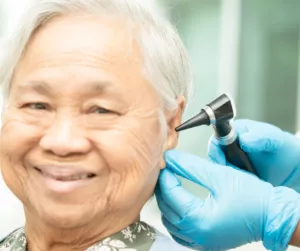 An older man smiles as gloved hands use an otoscope to look in his ear. 