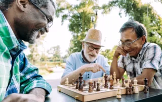 Three older men play chess together in a park.
