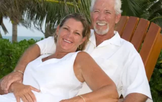 A smiling older couple poses together on a tropical vacation.