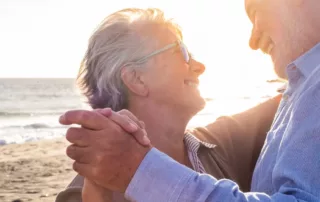 A smiling older couple dances together on a beach.