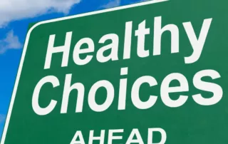 A highway sign says, “Healthy Choices Ahead,” and stands against a blue sky.