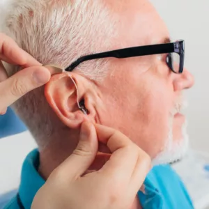 A hearing specialist fits a hearing on an older man.