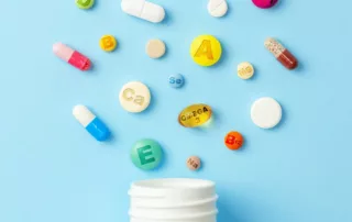 Different kinds of vitamins are on a blue background above a pill bottle.