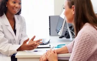 An audiologist talks to a patient at her desk.