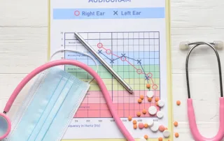 An audiogram, medications, and a scope sit on a white table.