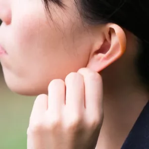 A woman pulls on her ear lobe to massage ear wax out. 