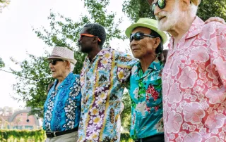 Four older men in Hawaiian shirts walk together outside.